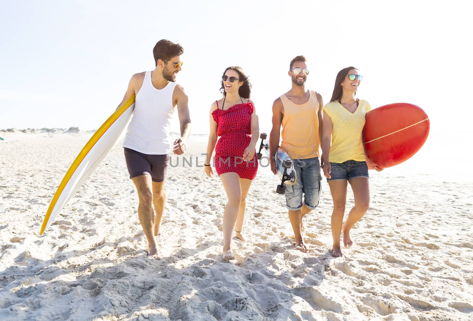Group of friends walking together at the beach and holding surfboards