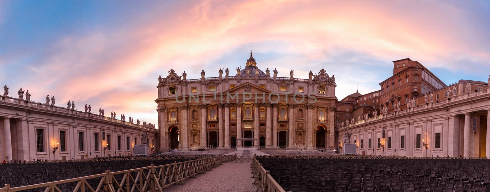 Front view of St Peter's Basilica in Vatican with people around, on cloudy blue sky backgroundat sunset time.