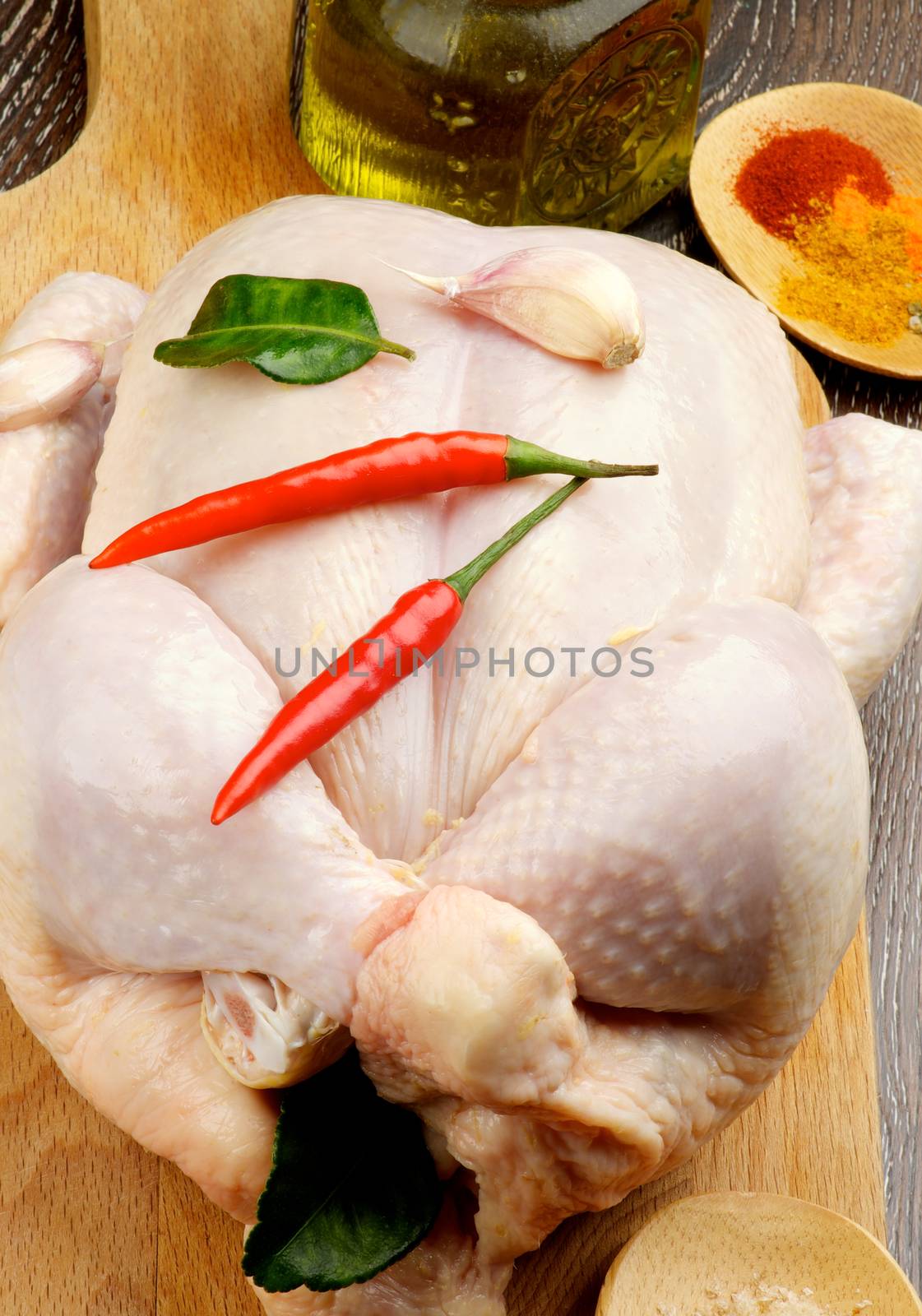 Big Raw Chicken Full Body Trussed and Ready to Roast with Hot Crushed Spices, Chili Peppers, Garlic and Olive Oil closeup on Wooden Cutting Board