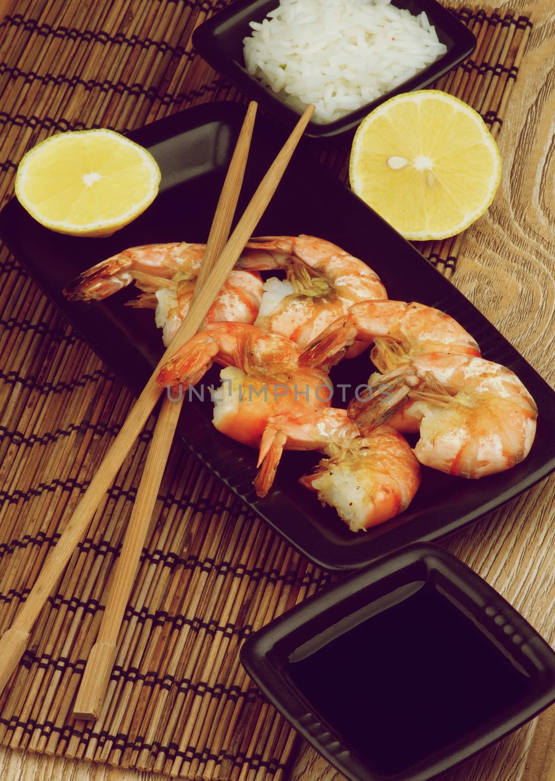 Delicious Roasted Shrimps with Soy Sauce, Boiled Rice, Lemons and Chopsticks in Asian Style closeup Straw Mat background