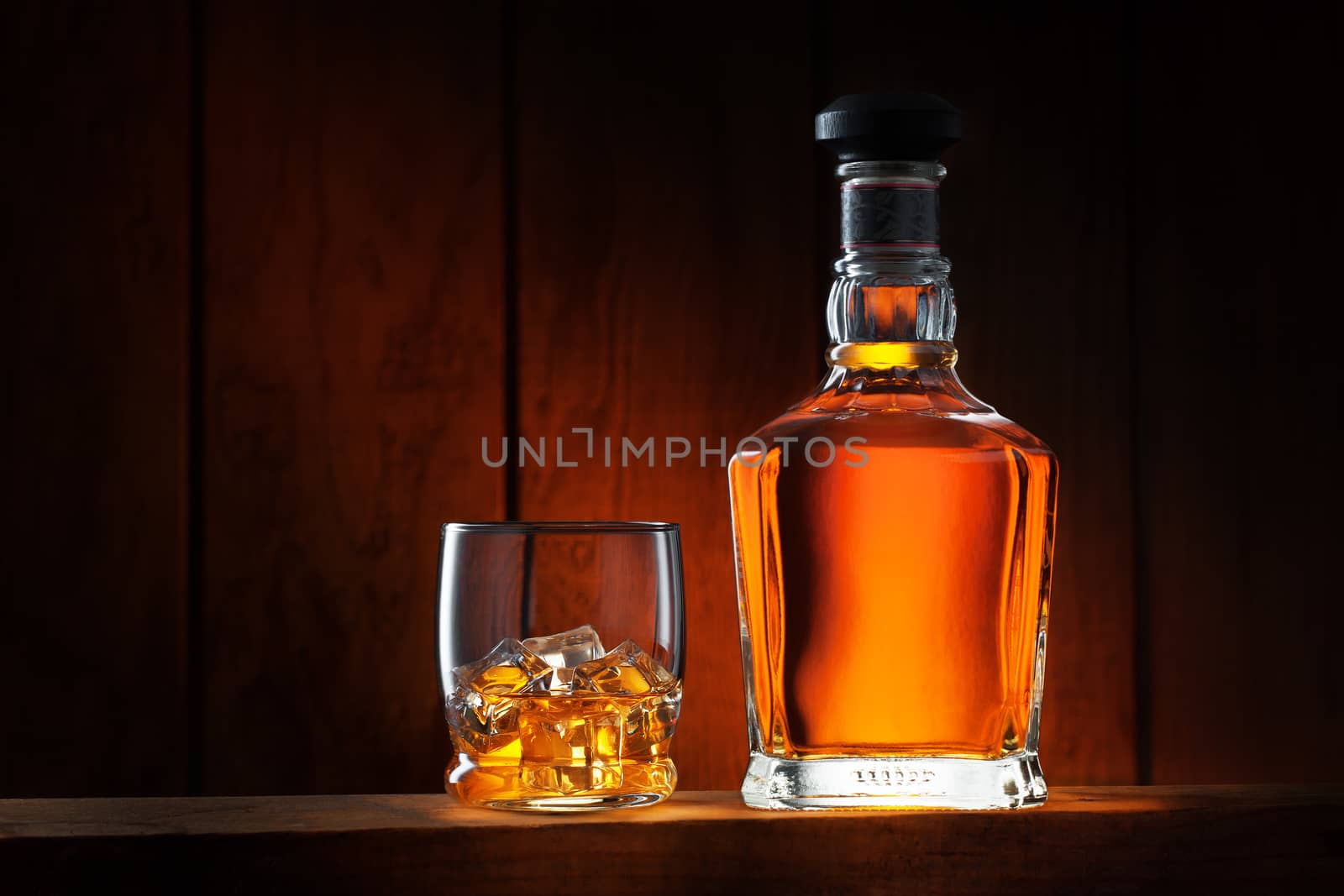 close up view of glass with ice and whiskey and a bottle aside