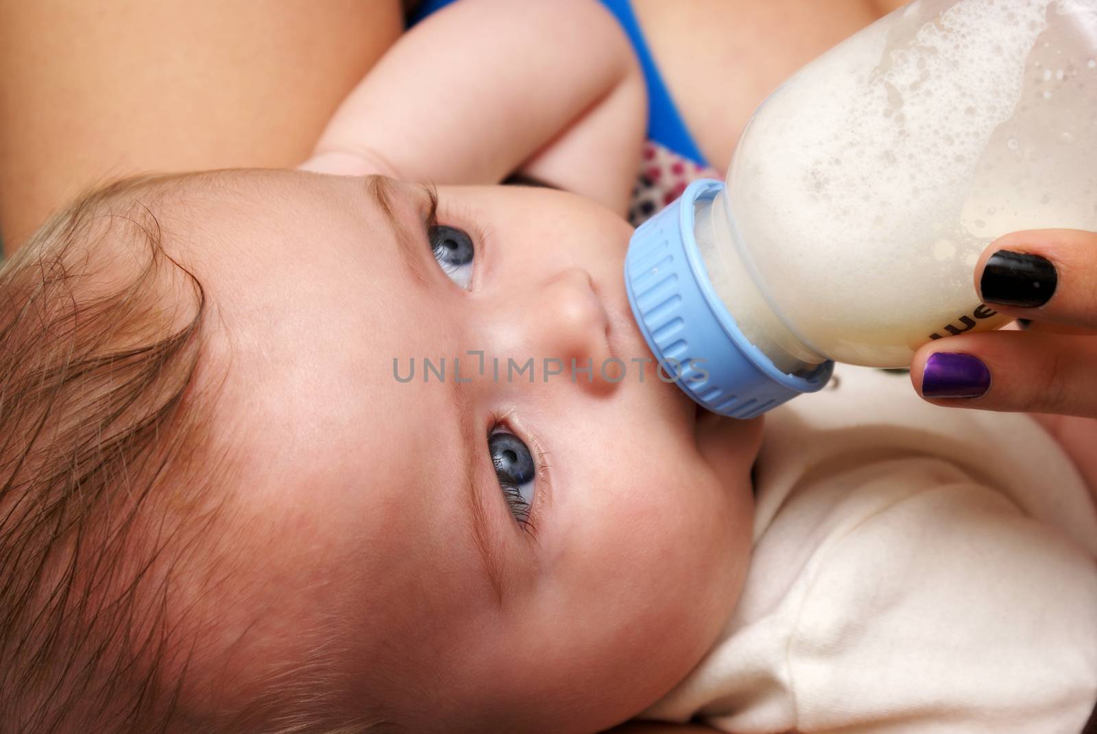 A closeup view of a mother feeding her handsome five month old son a bottle of formula.