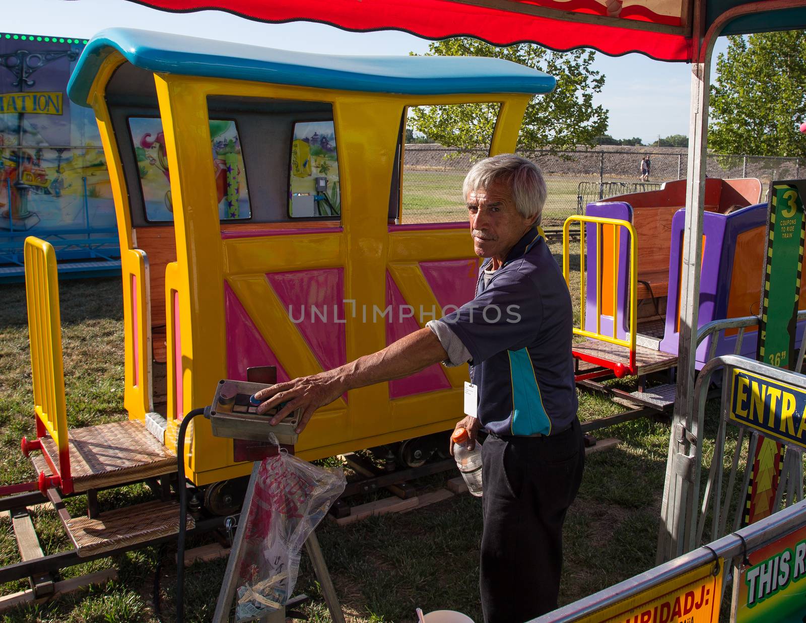 Anderson, California, USA- June 17, 2015: A carnival train employee operates equipment that drives a toy train with children at the Shasta County fair.He operates the ride with the push button control at his fingertips.