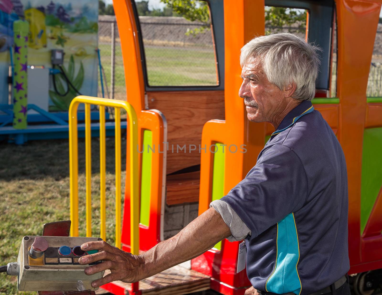 Anderson, California, USA- June 17, 2015: A carnival train employee operates equipment that drives a toy train with children at the Shasta County fair.He operates the ride with the push button control at his fingertips.