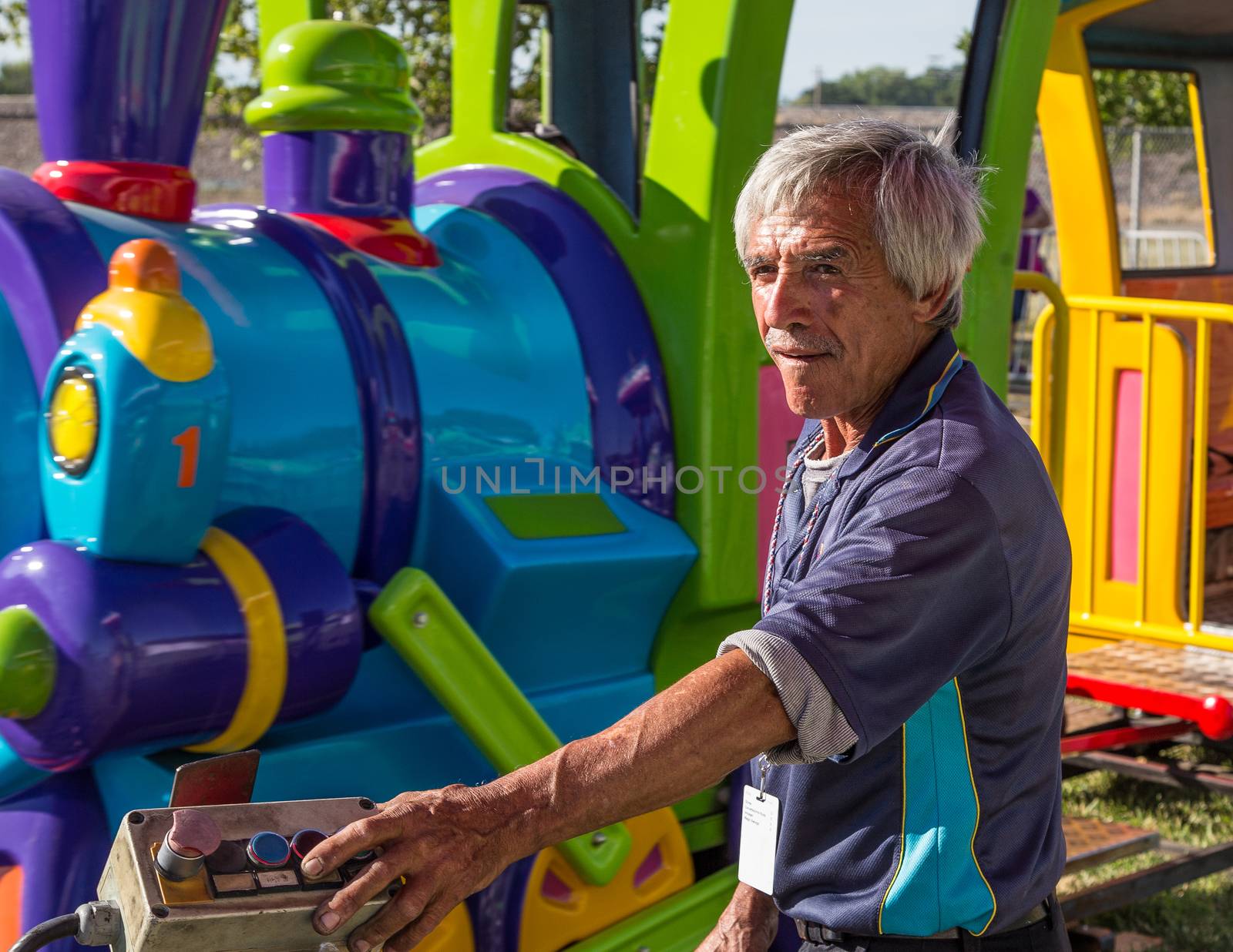 Anderson, California, USA- June 17, 2015: A carnival train employee operates equipment that drives a toy train with children at the Shasta County fair.He operates the ride with the push button control at his fingertips.