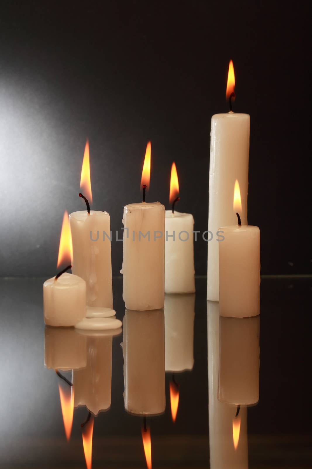 Few lighting candles with reflection on dark background