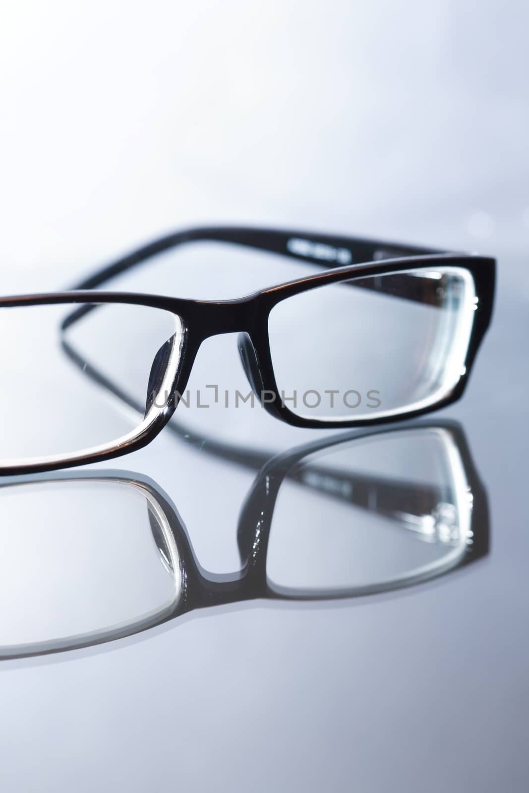 Modern black eyeglasses on glass surface against gray background