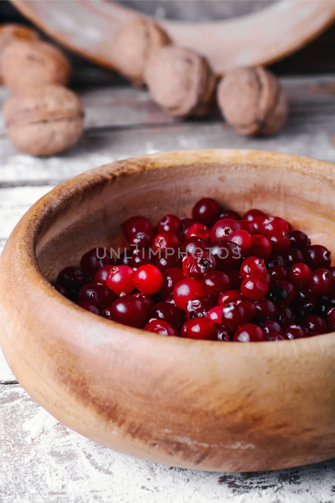 Wooden bowl with cranberries on a wooden background with kitchen smeared with flour
