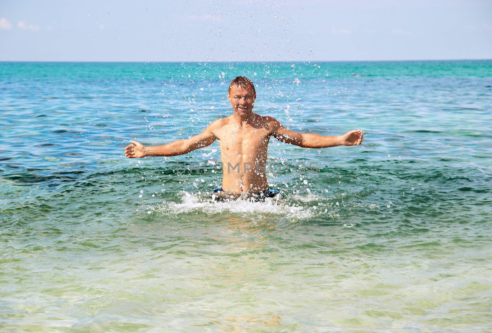 Happy man in the tropical sea with splashes