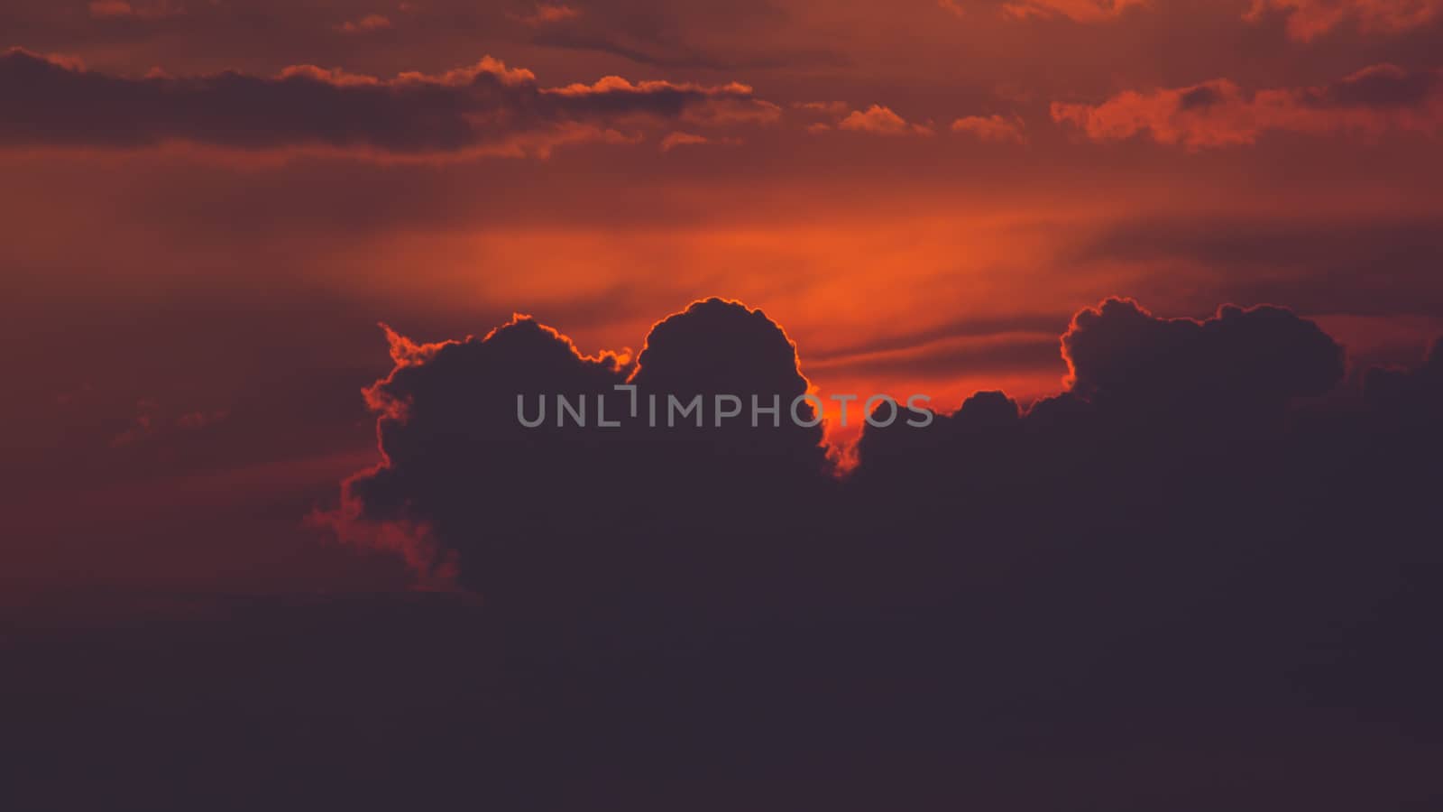 Warm coloured sky before dusk, Sun sheltered behind giant cloud.