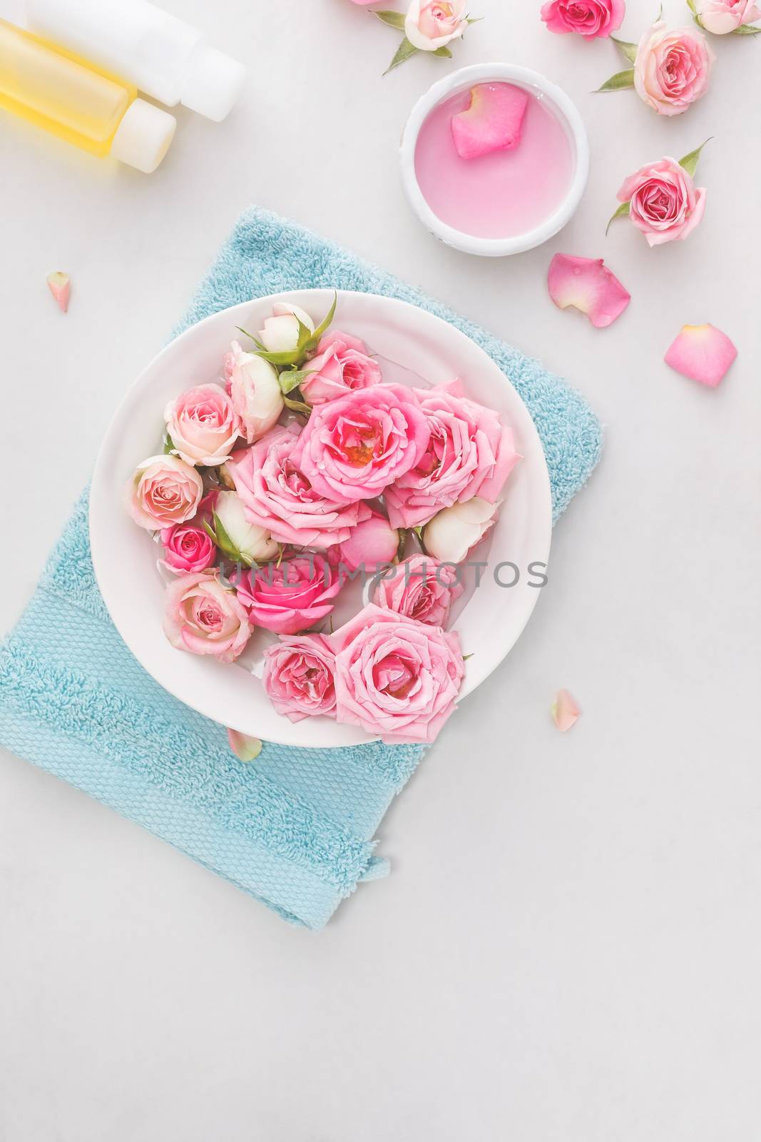 Fresh roses and rose petals in a bowl of water and various items used in spa treatments
