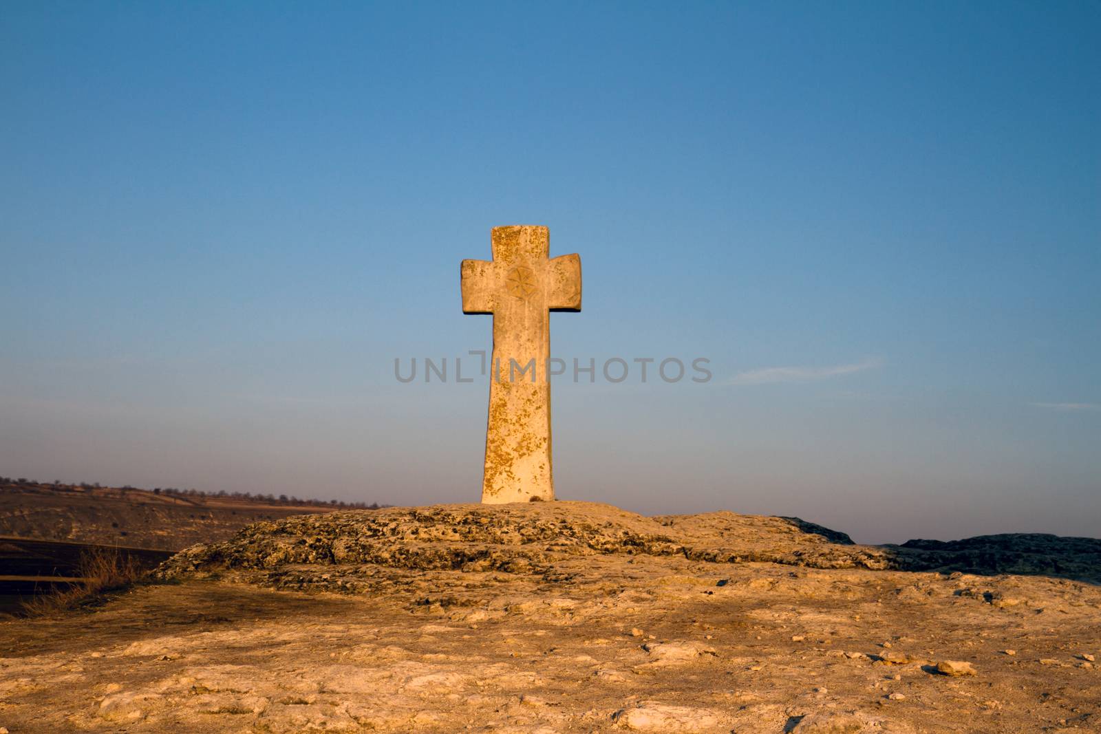 Ancient Christian stone cross on the hill with blurred fields in the background and blue sky, Old Orhei place in Moldova.