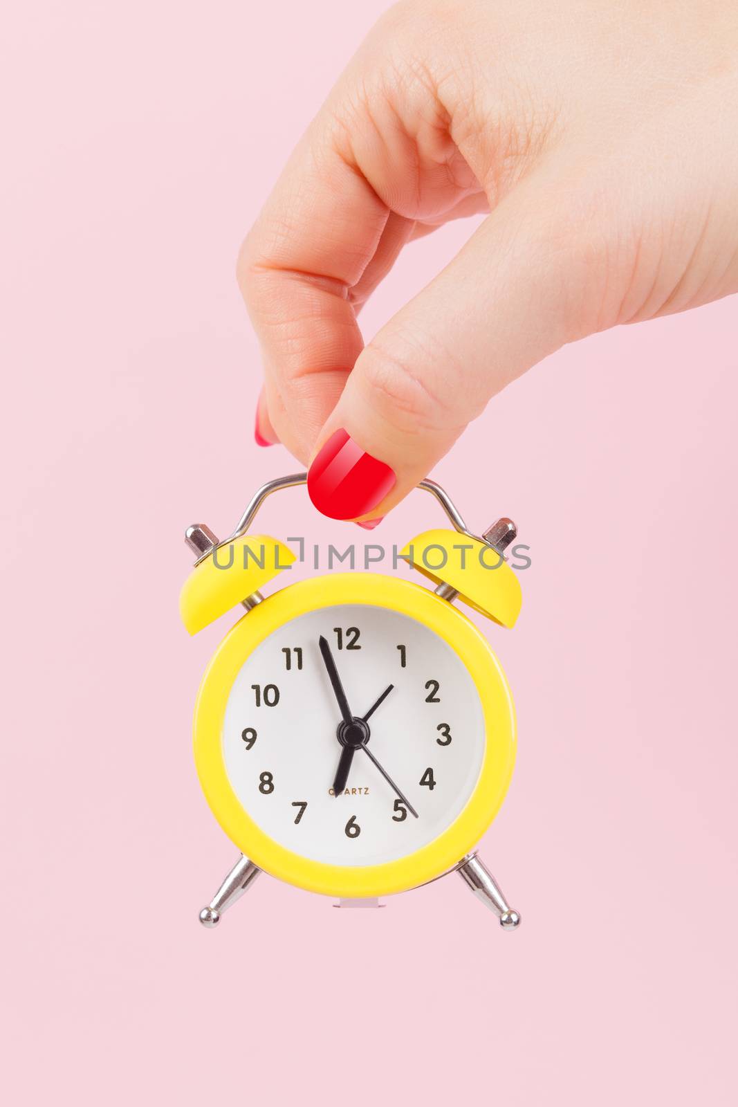 Female hand with yellow alarm clock on pink background. Deadline. Running late. Just in time. Time concept. 