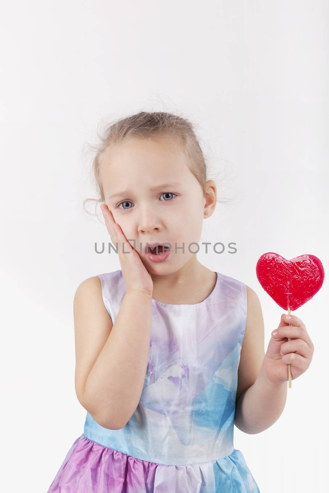 Toothache. Little girl with lollypop and hurt teeth holding her cheek.