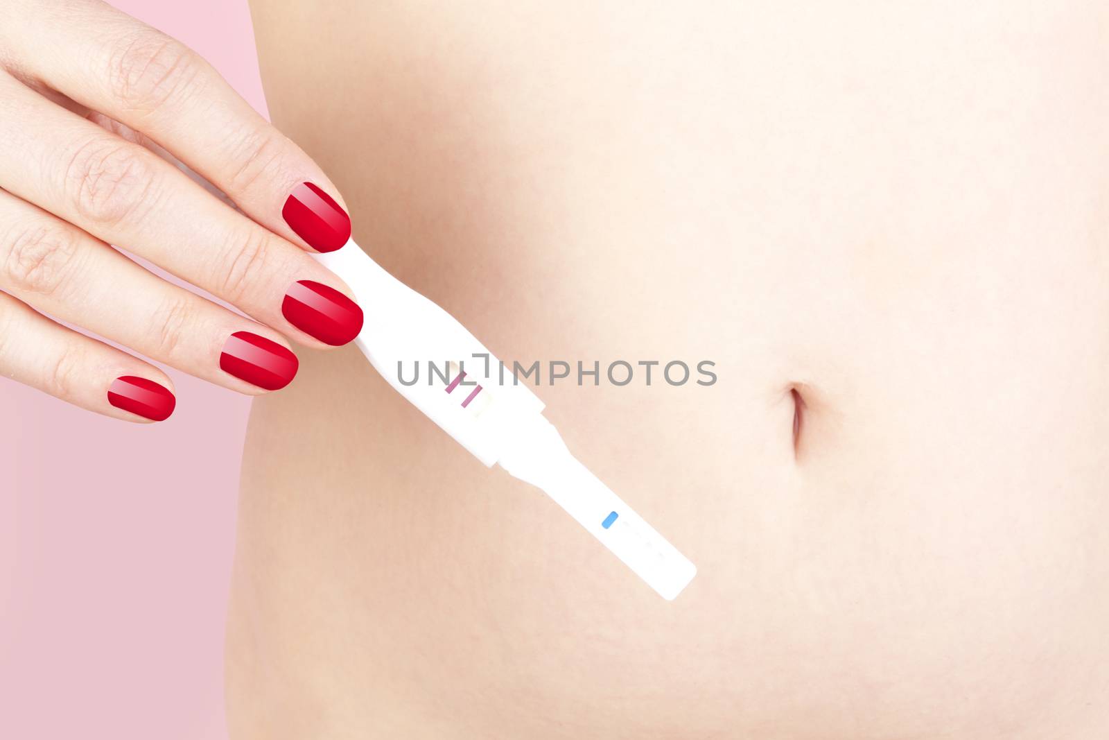 Sexy woman with red nails holding pregnancy test against her belly. Maternity and pregnancy test.