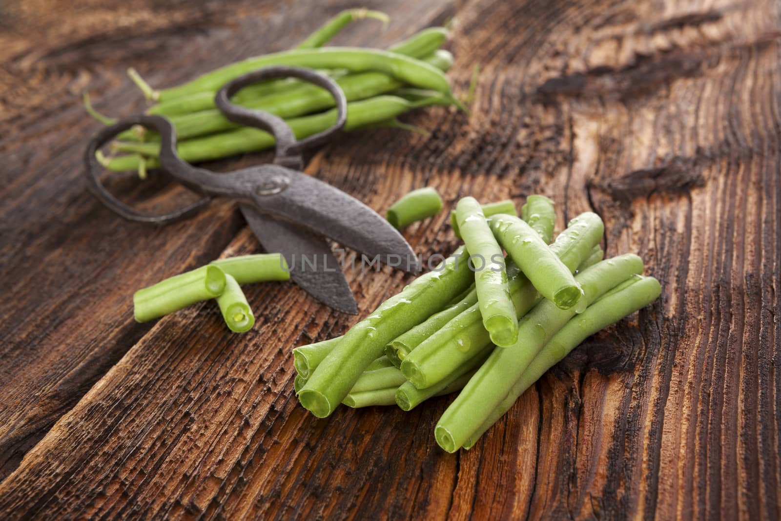 Raw fresh green beans with water drops on brown wooden textured table. Fresh vegetable eating. 