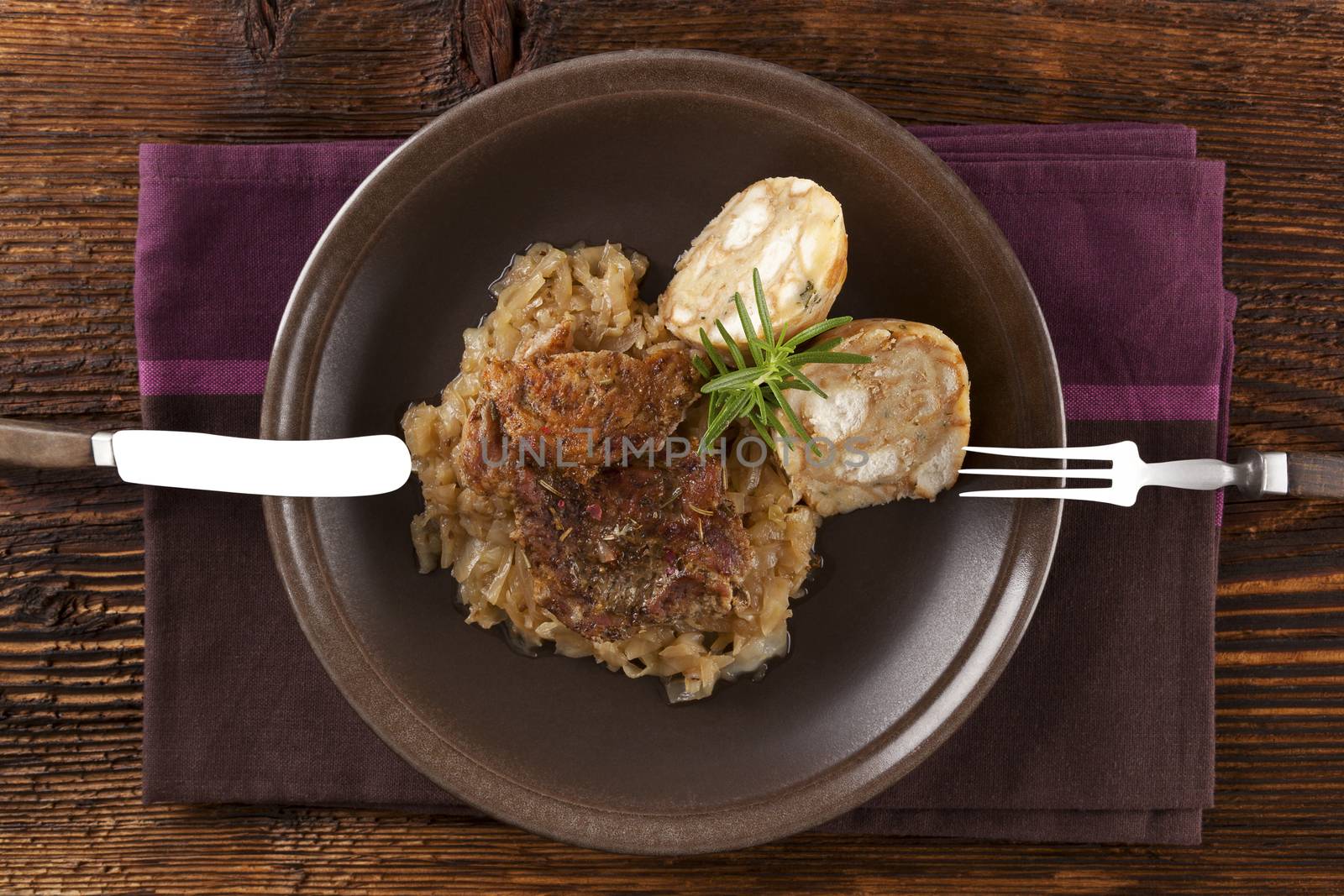 Baked pork chop with dumplings and sauerkraut on plate with silver cutlery on wooden table, top view. 