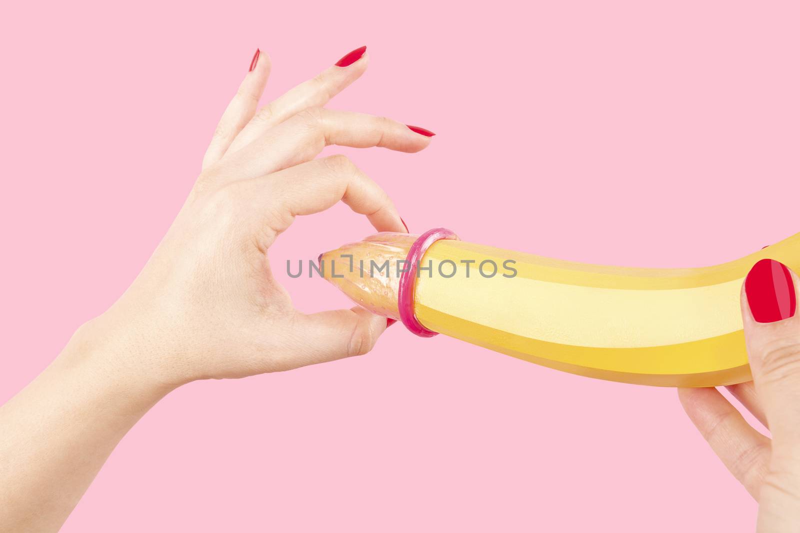 Female hand with red fingernails puts on a condom onto a banana. Safe sex concept.