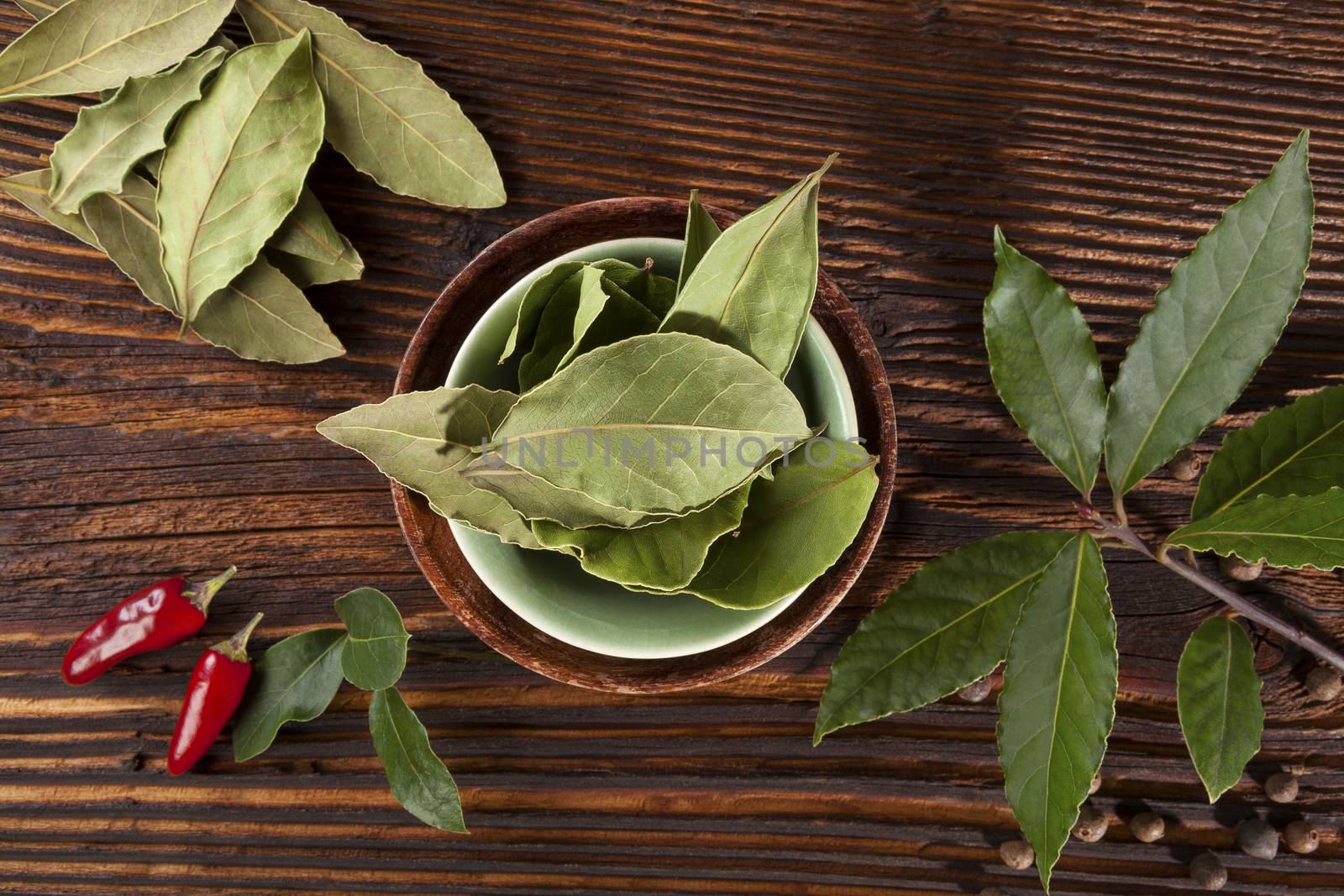 Bay leaves, traditional spice and condiment wooden background. Bay leaves, rosemary, chillies and black pepper on brown wooden table, top view.