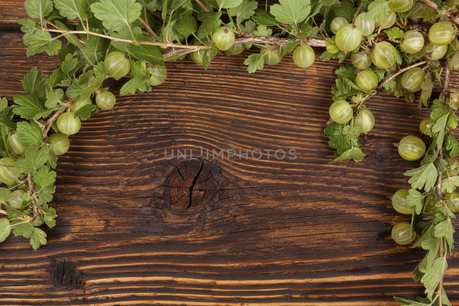 Green gooseberries with green leaves on wooden vintage table, top view. Healthy summer fruit eating. 