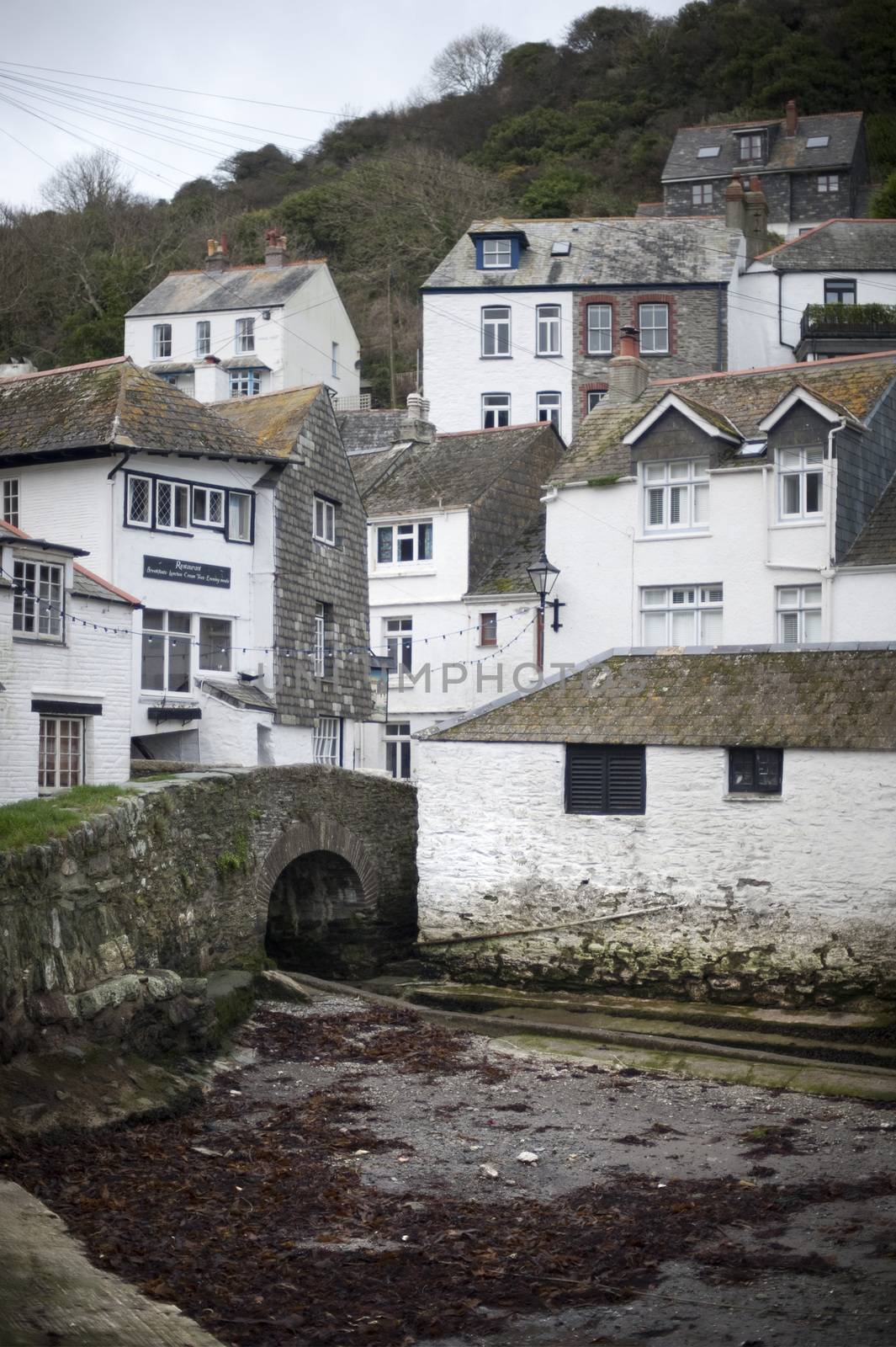 Desolate Polperro fishing village in Cornwall with little stream and stone bridge near bottom of hill next to buildings