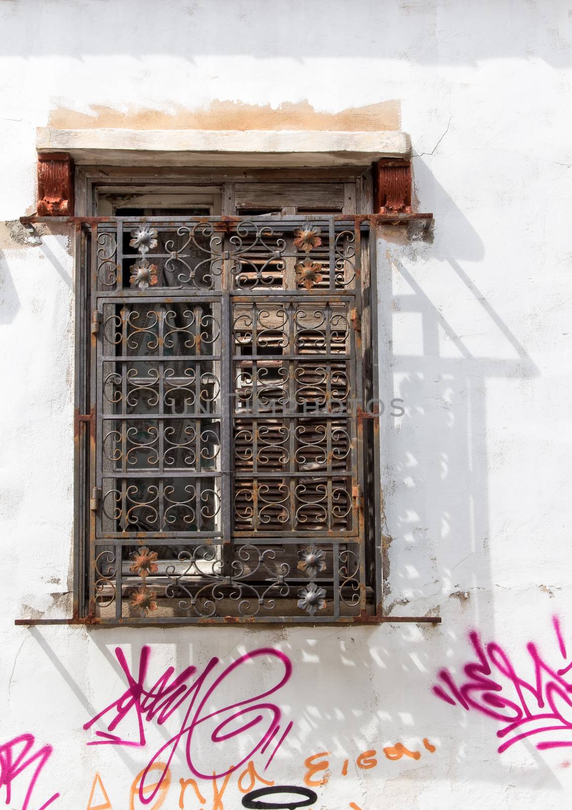 Old destroyed window with ornate lattice. White facade of the house with graffiti. Athens. Greece.