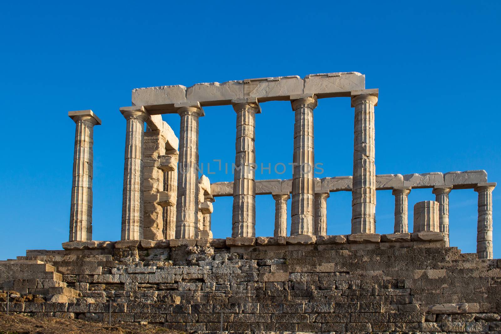 Golden hour light on the columns of Poseidon temple in Cape Sounion, Greece. Bright blue sky.