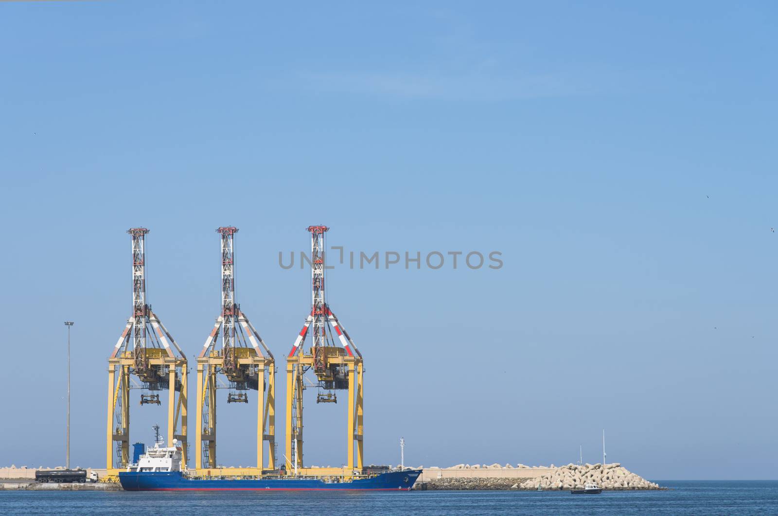 Small oil tanker moored at a breakwater with three container cranes.