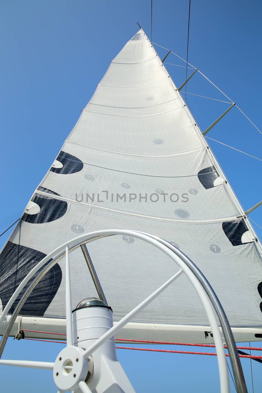 The mast, sail and rudder of the yacht on the background of blue sky