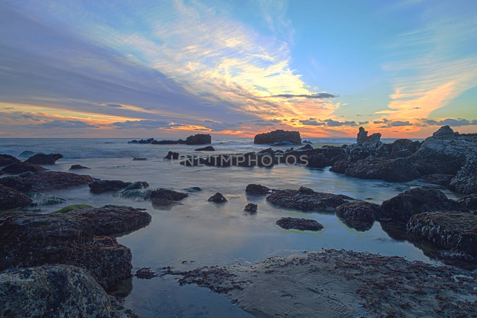 Long exposure of sunset over rocks, giving a mist like effect over ocean in Laguna Beach, California, United States