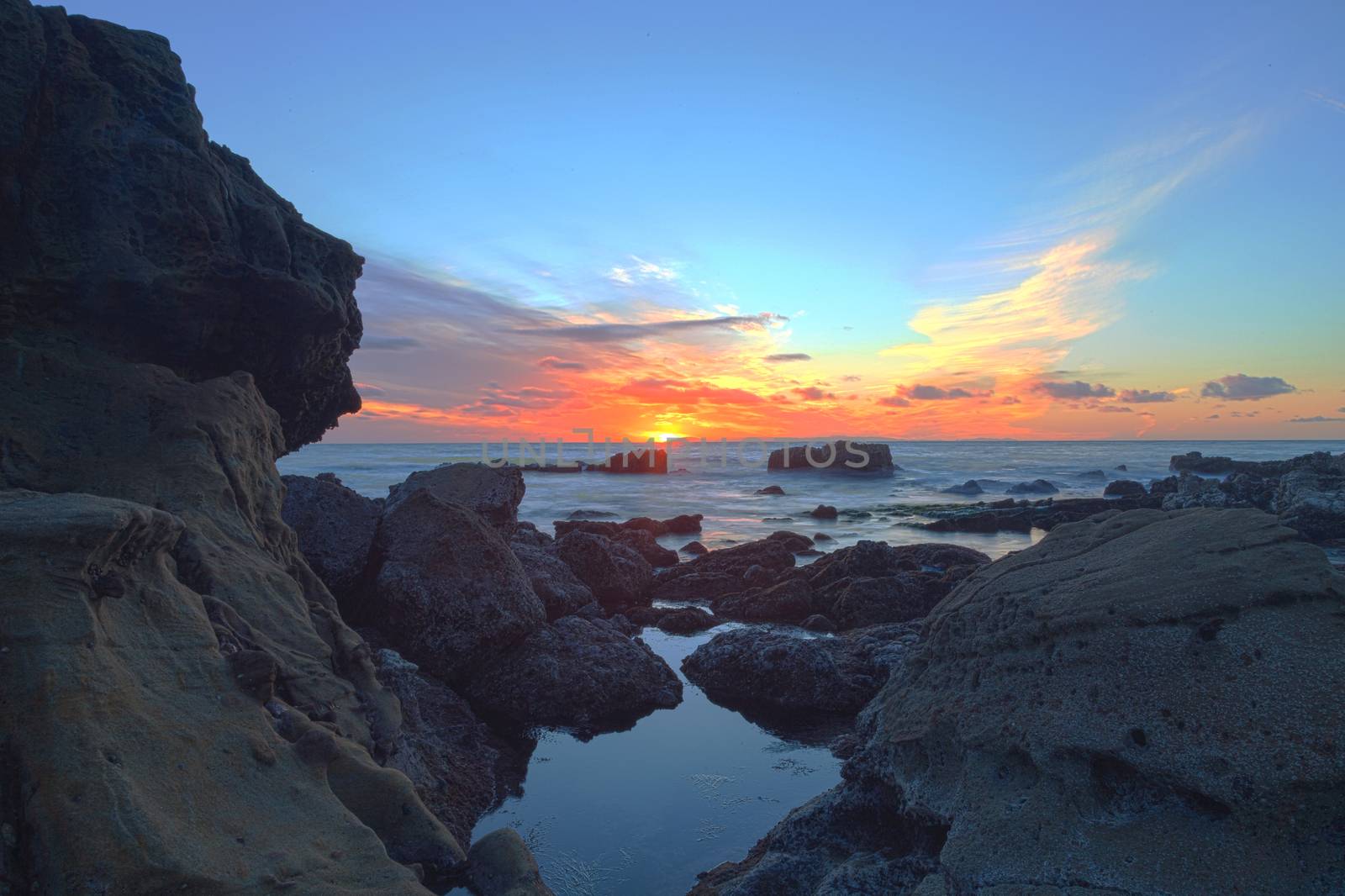 Long exposure of sunset over rocks, giving a mist like effect over ocean in Laguna Beach, California, United States