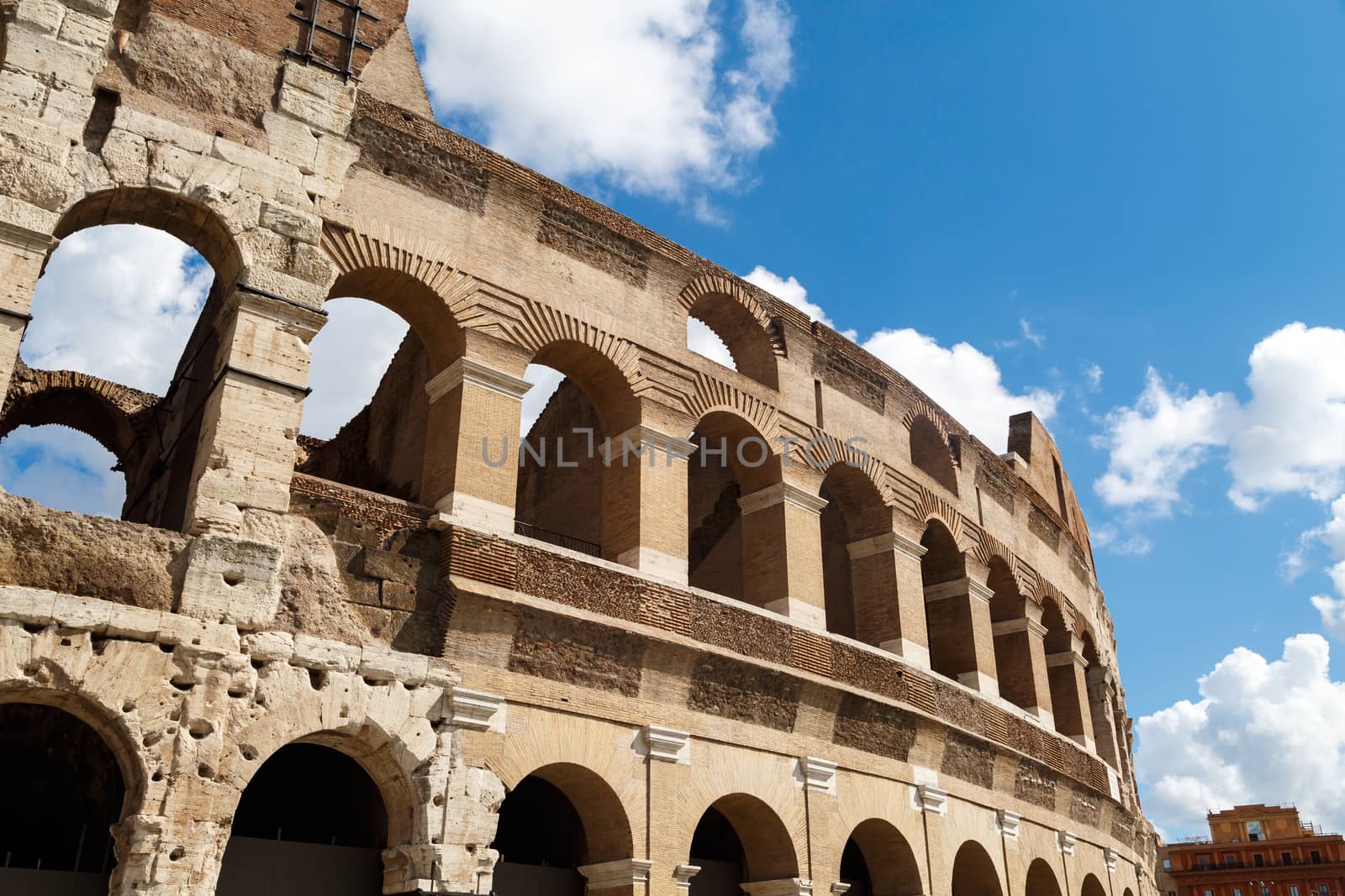 Close up detailed view of ancient amphitheatre of Colosseum built by Vespasian and Titus in Rome, on cloudy blue sky background.