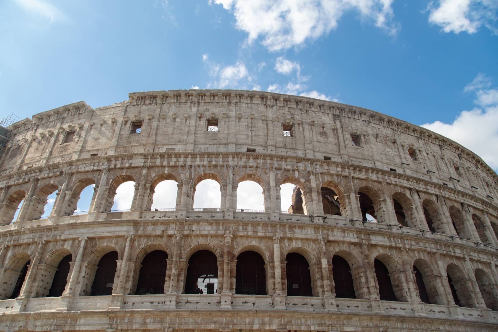 Bottom view of ancient amphitheatre of Colosseum built by Vespasian and Titus in Rome, on cloudy blue sky background.