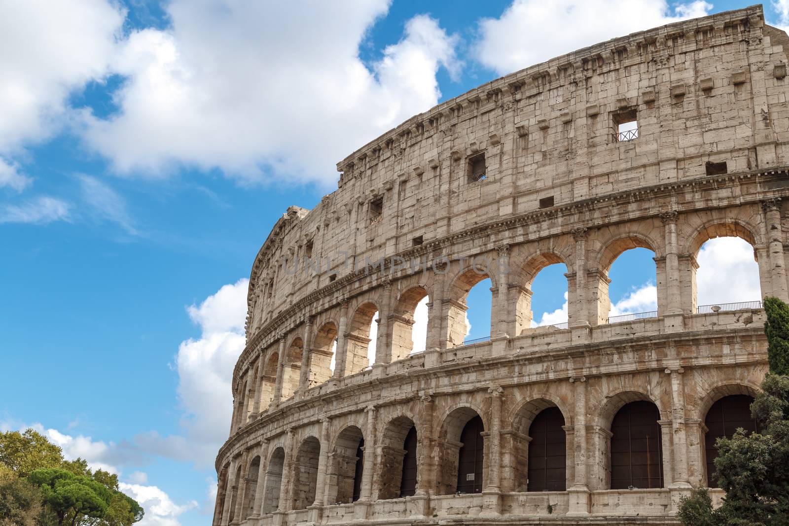Close up detailed view of ancient amphitheatre of Colosseum built by Vespasian and Titus in Rome, on cloudy blue sky background.