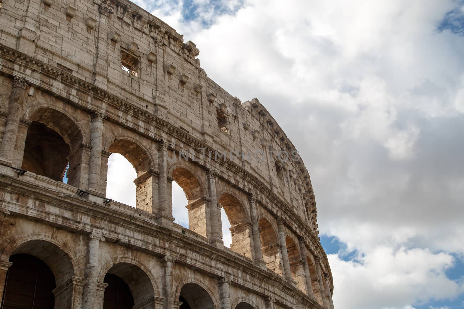 Close up detailed view of ancient amphitheatre of Colosseum built by Vespasian and Titus in Rome, on cloudy sky background.