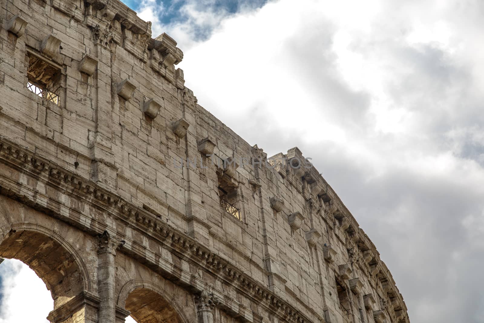 Close up detailed view of ancient amphitheatre of Colosseum built by Vespasian and Titus in Rome, on cloudy sky background.