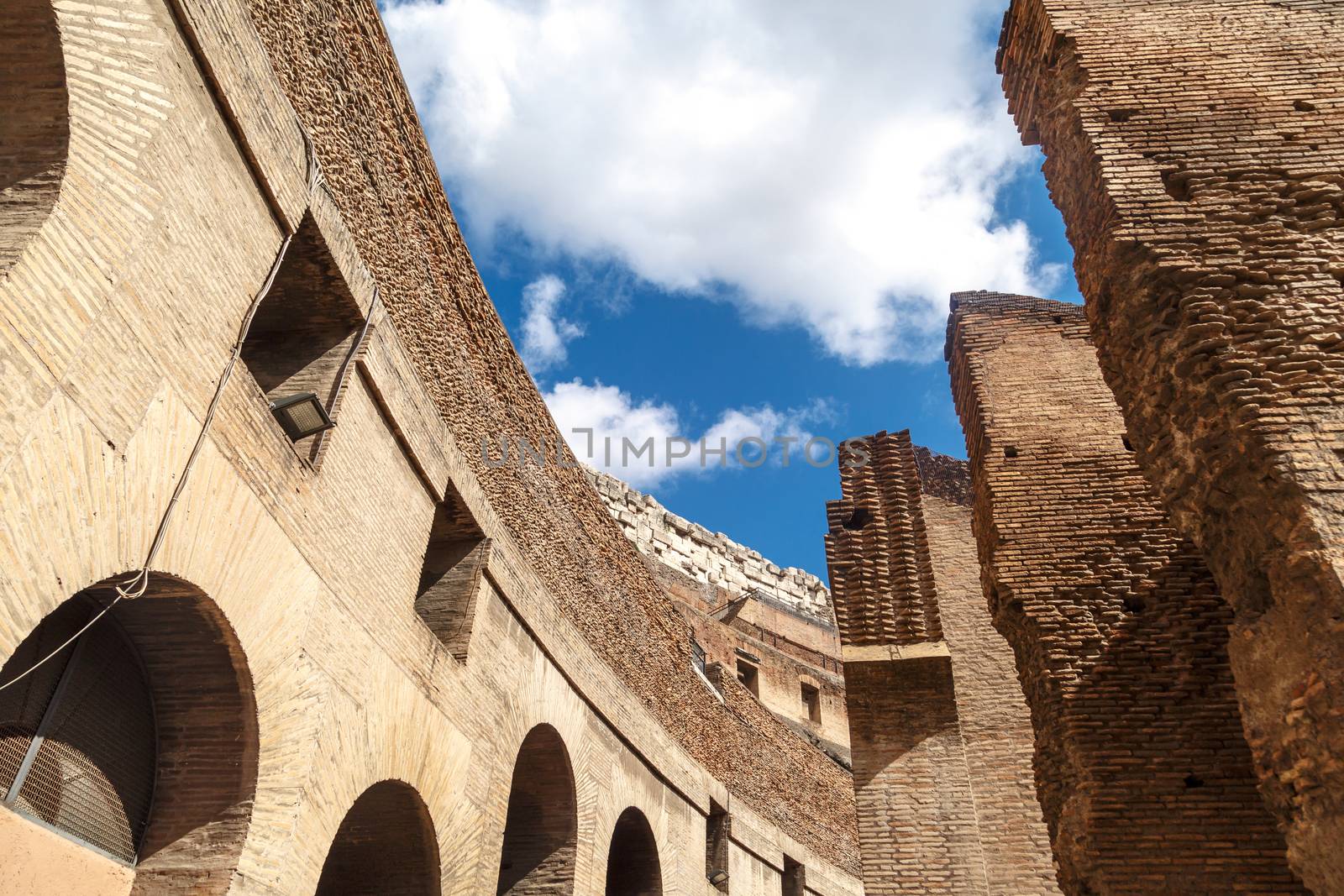 Close up detailed inside view of ancient amphitheatre of Colosseum built by Vespasian and Titus in Rome, on cloudy blue sky background.