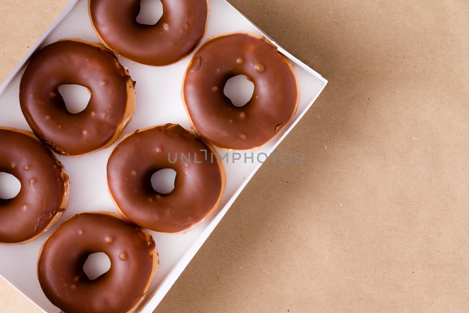 First person perspective top down view of six chocolate and cream donuts in open box over brown table with copy space