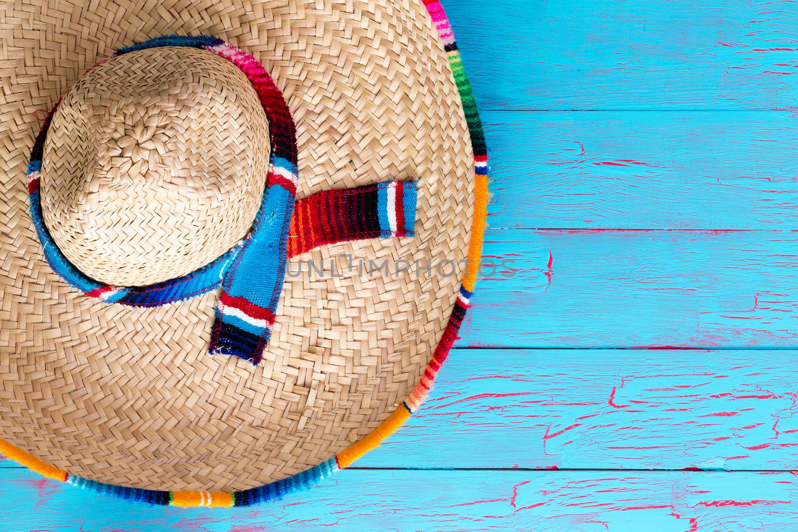 Colorful wide brimmed straw sombrero with multicolor trim and ribbon lying on a bright blue picnic table with copy space conceptual of summer travel