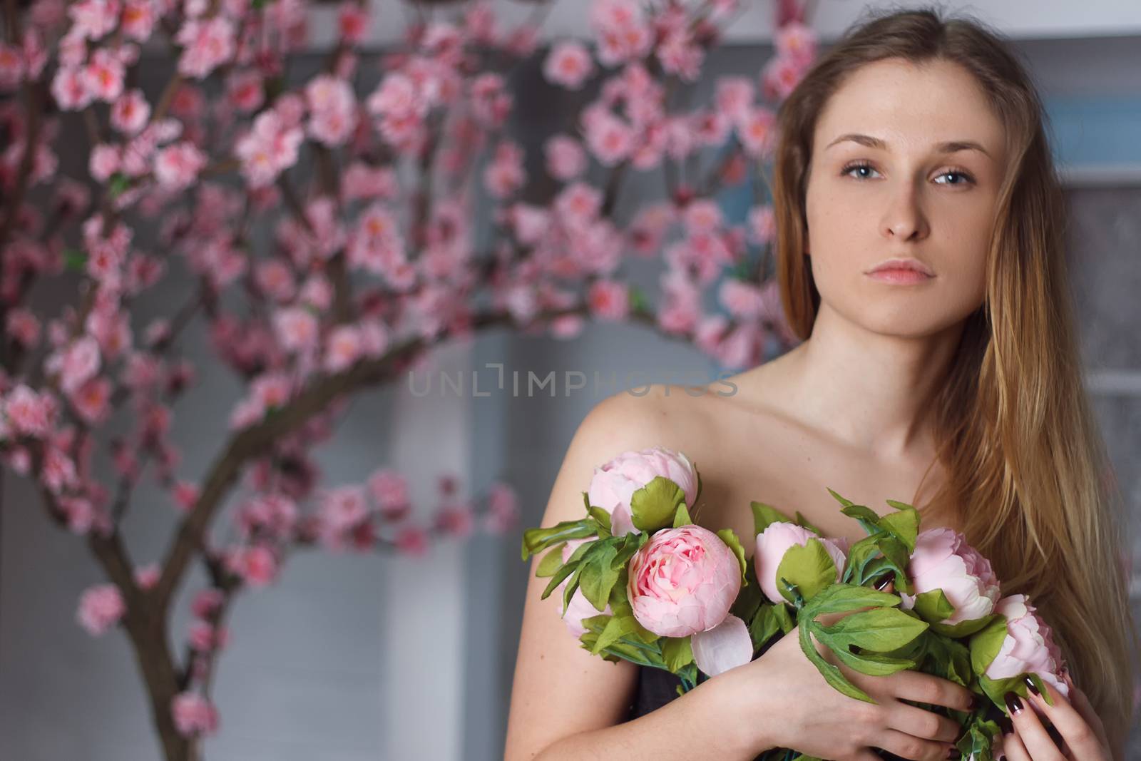Beautiful close-up portrait of a young woman with peonies wreath. Spring natural care concept.
