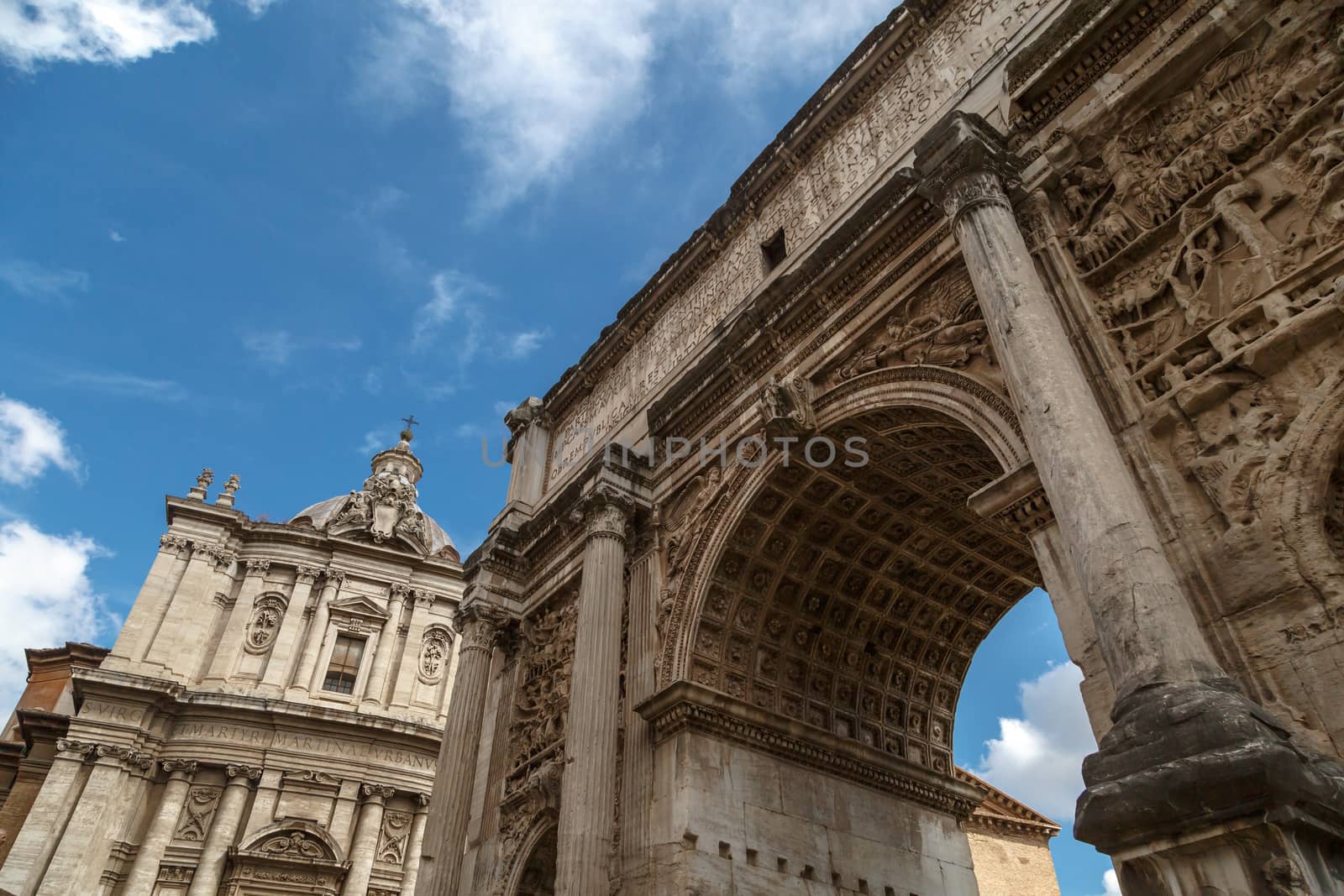 Bottom view of ancient arch with columns at Roman Forum, on cloudy blue sky background.