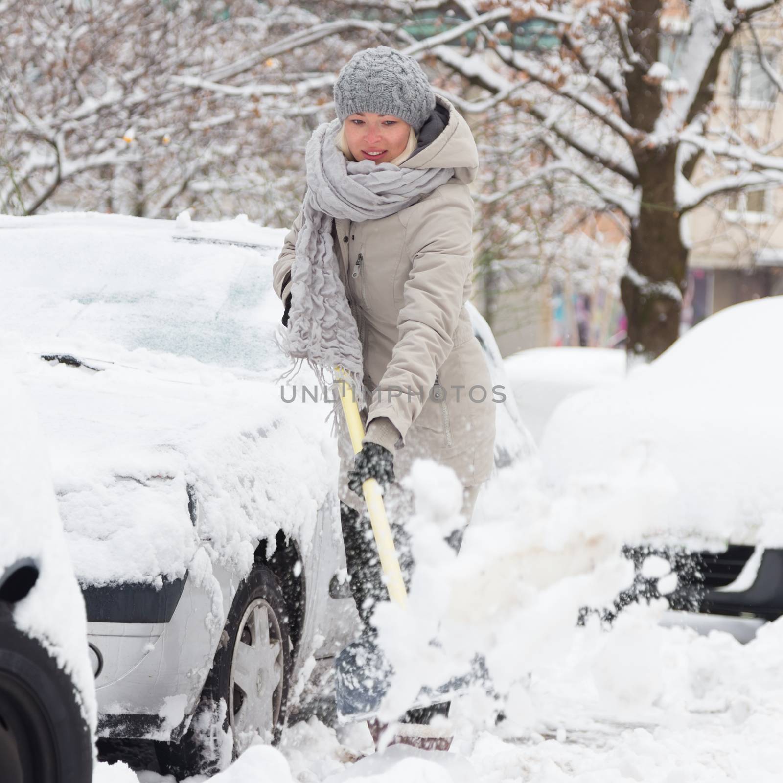 Independent woman shoveling her parking lot after a winter snowstorm.