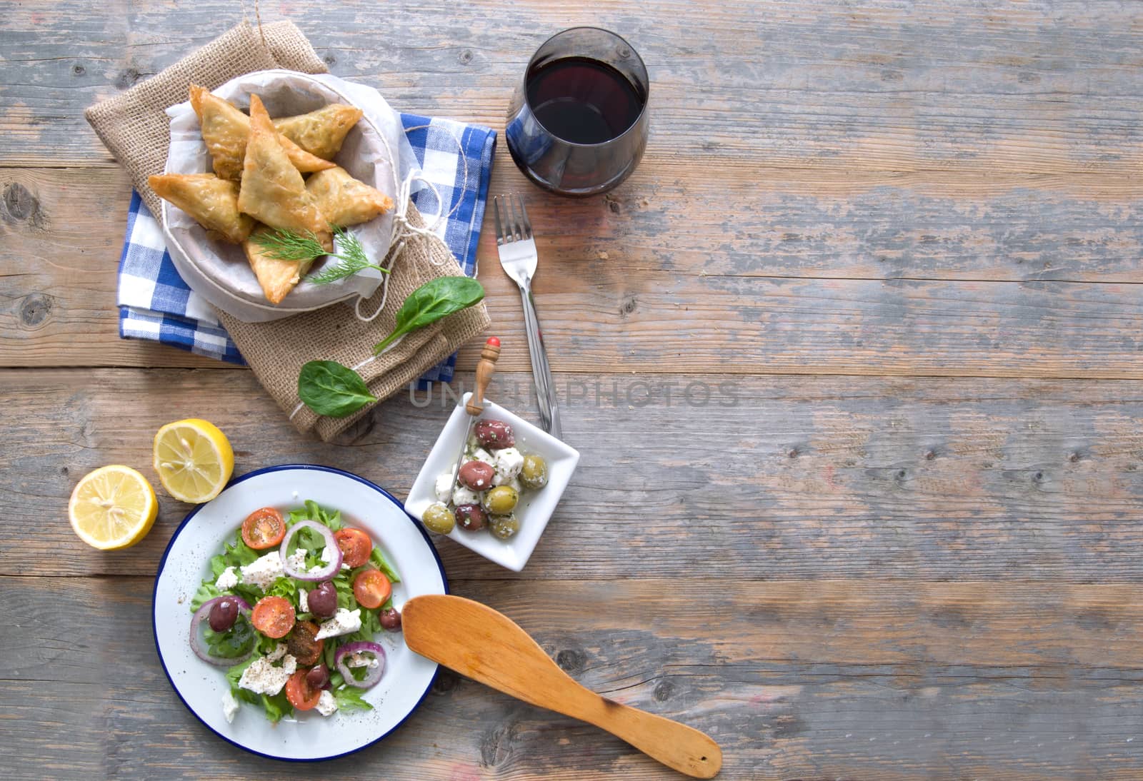 Feta cheese and spinach filo pastries and greek salad laid out on a wooden table