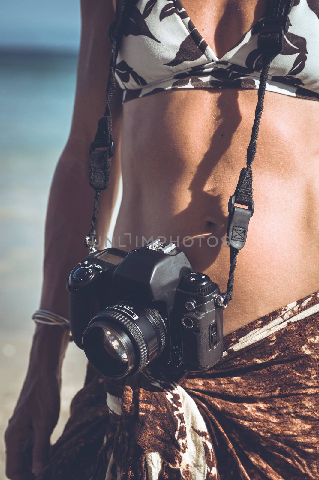 Woman on a tropical beach with an film camera around her neck.