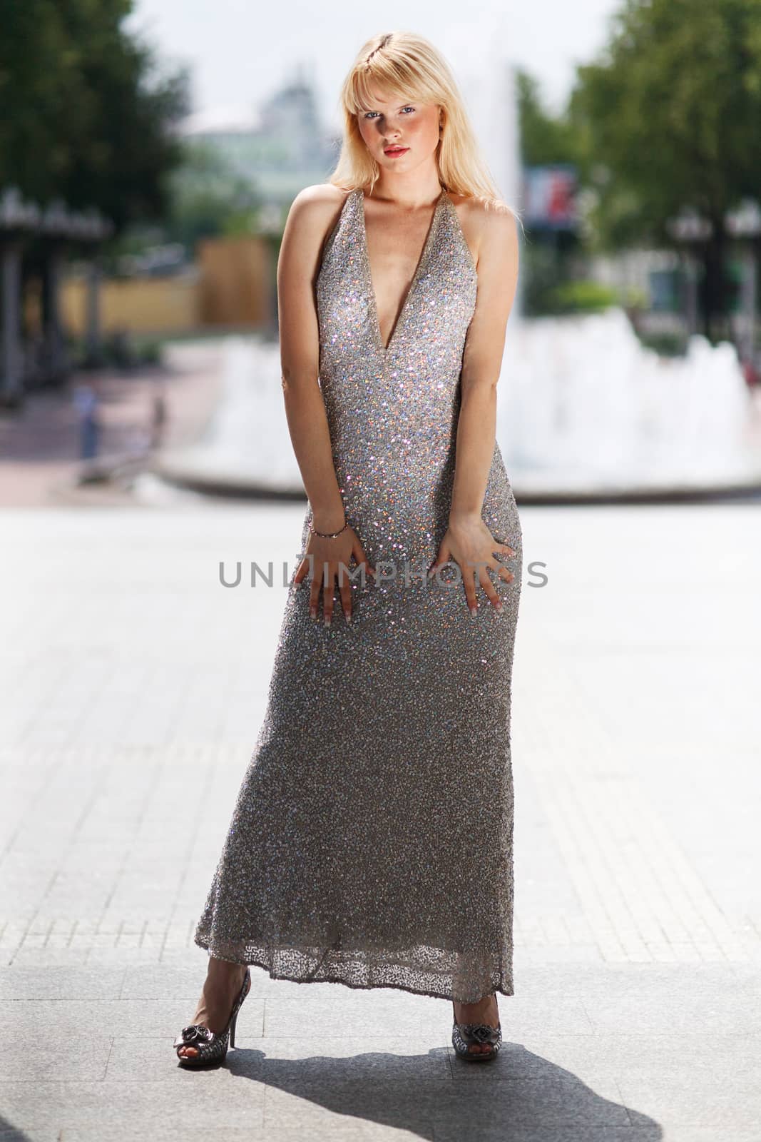 Blond stand woman in glitter dress next to fountain