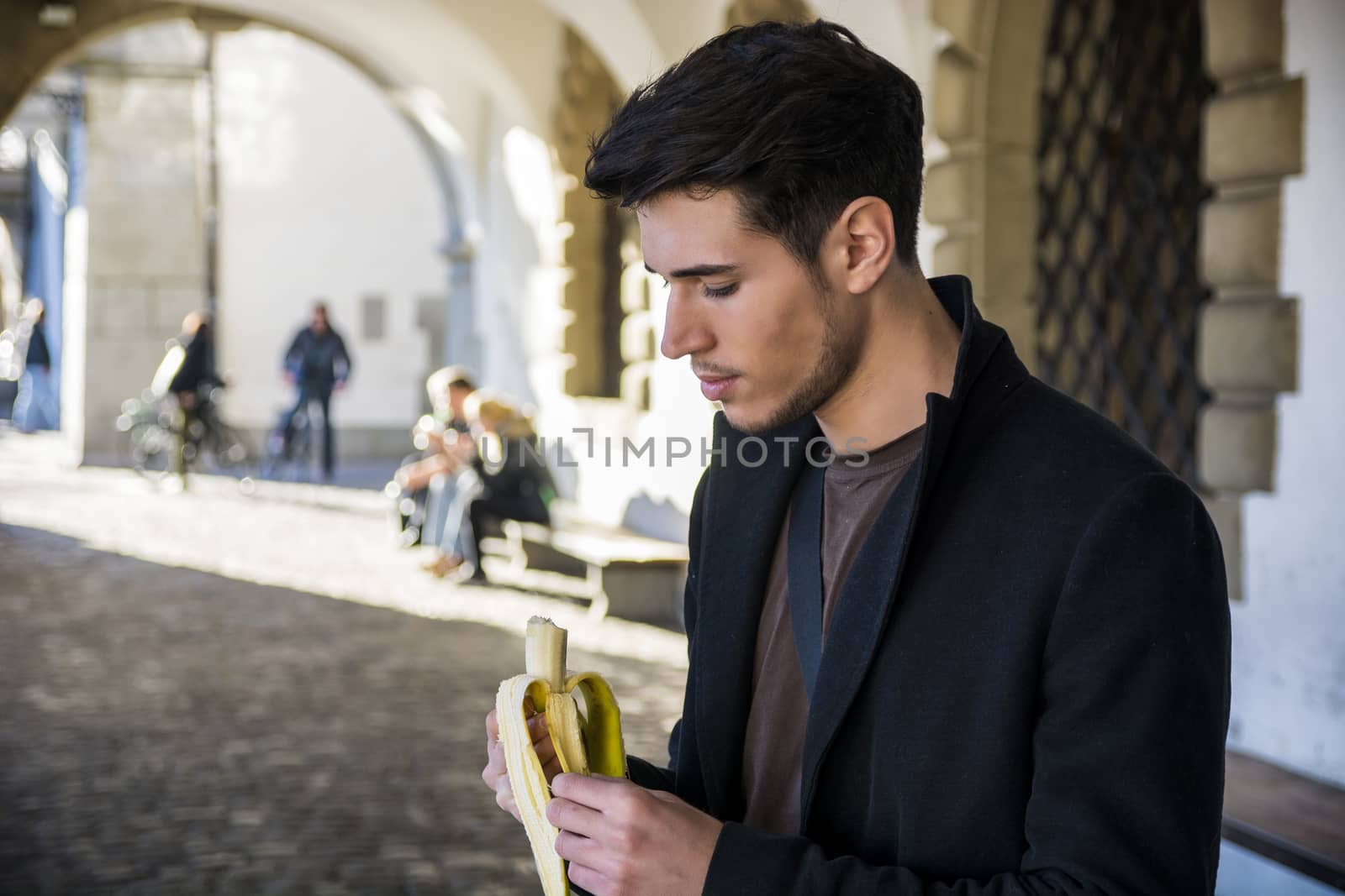 Man with banana standing on street in Lausanne while looking down by artofphoto