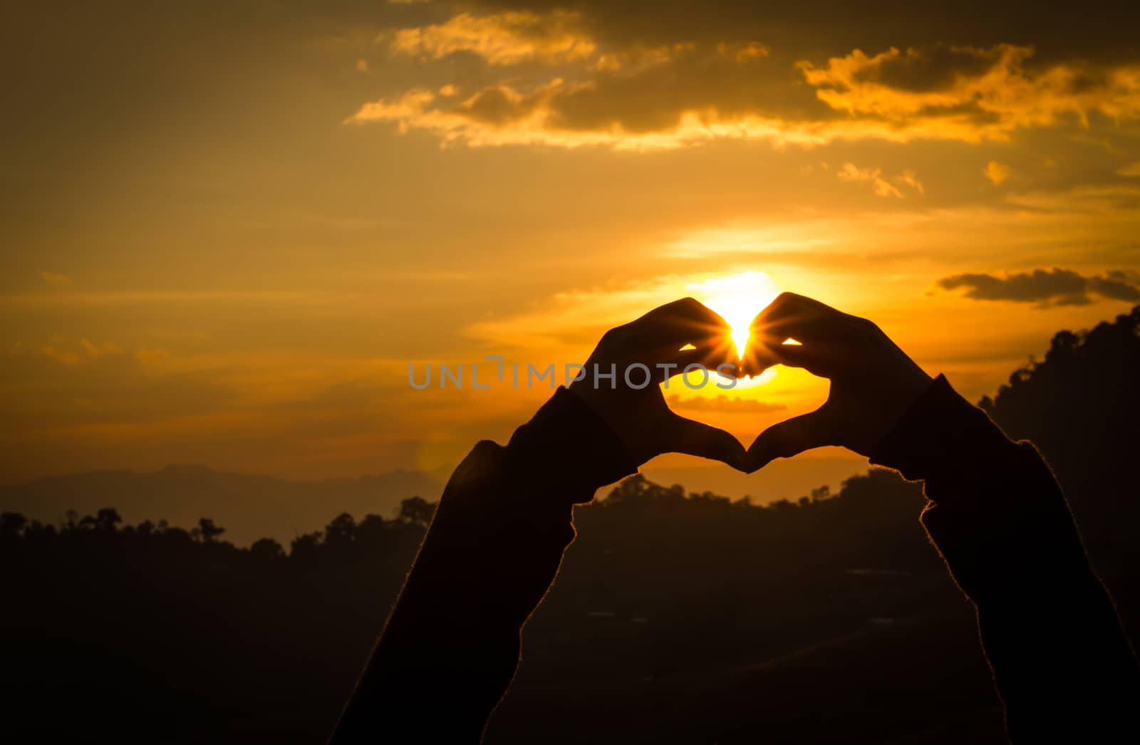 Silhouettes hand heart shaped with sun sets and the sky orange