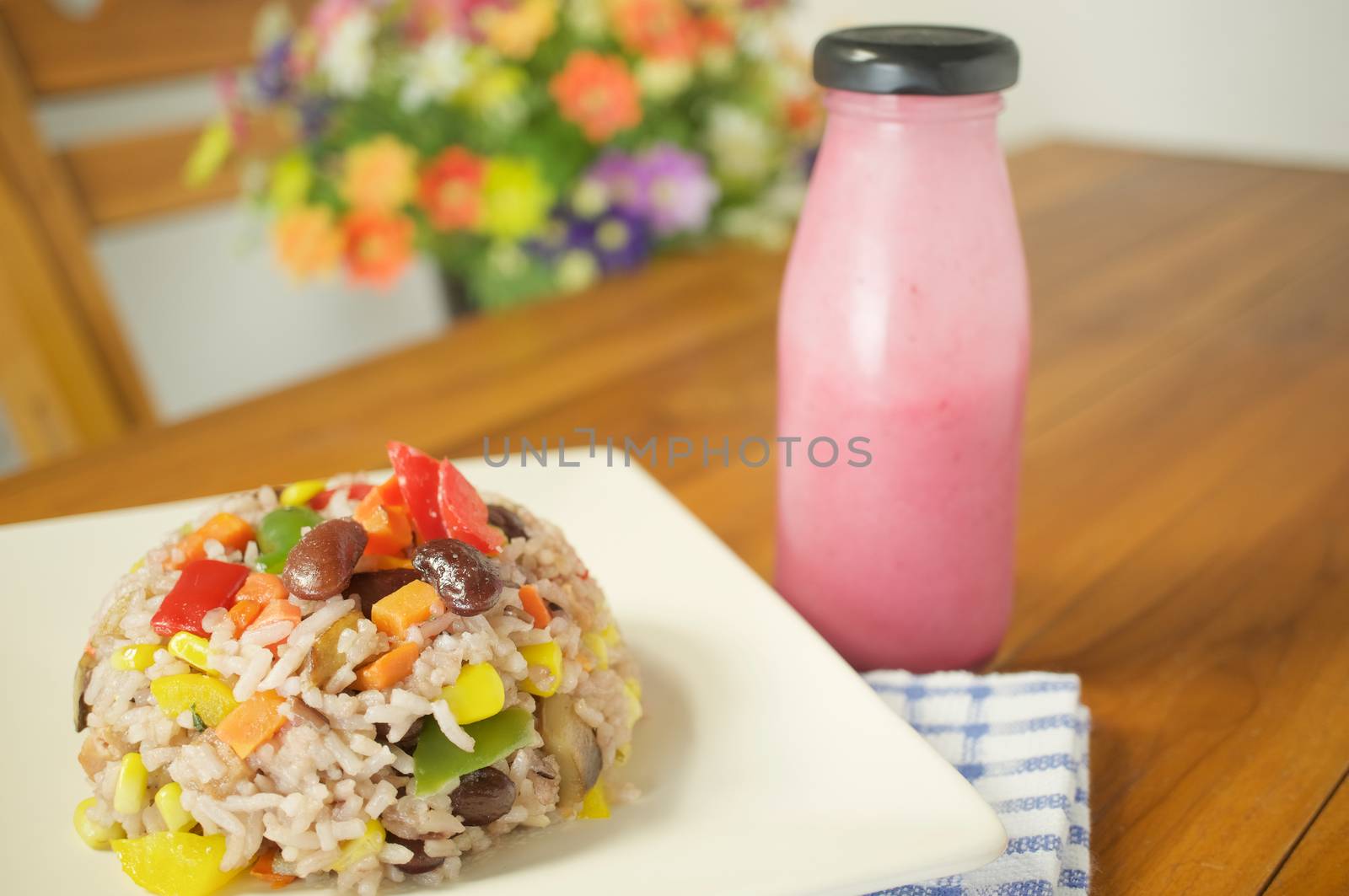 Fried rice vegetarian include eringi mushrooms carrots and corn with blue fabric and salad dressing on wood table and blur flower as background.