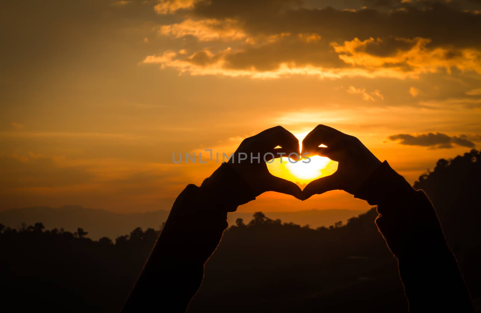 Silhouettes hand heart shaped with sunsets and the sky orange.