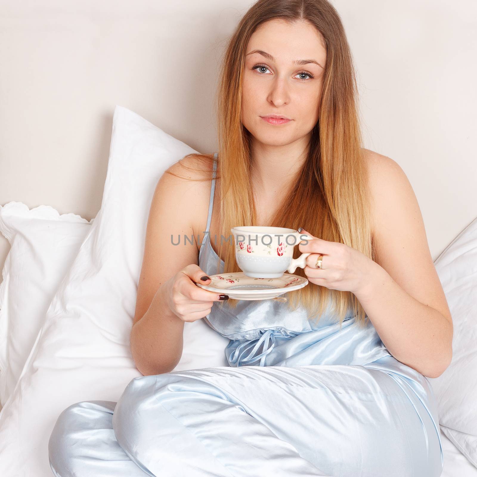 Woman in pajamas holding cup of teaon her bed